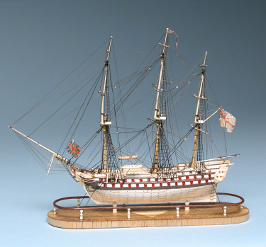   PRISONER-OF-WAR BONE MODEL OF A TRIPLE-DECKER SHIP-OF-THE-LINE, circa 1800, with seventy-eight guns run-out, carved male figurehead, engraved and polychromed stern-castle, wooden highlights, and cloth British ensigns flying at bow, masthead and stern; mounted on marquetry inlaid base. Height 19  in. Length 21  in.